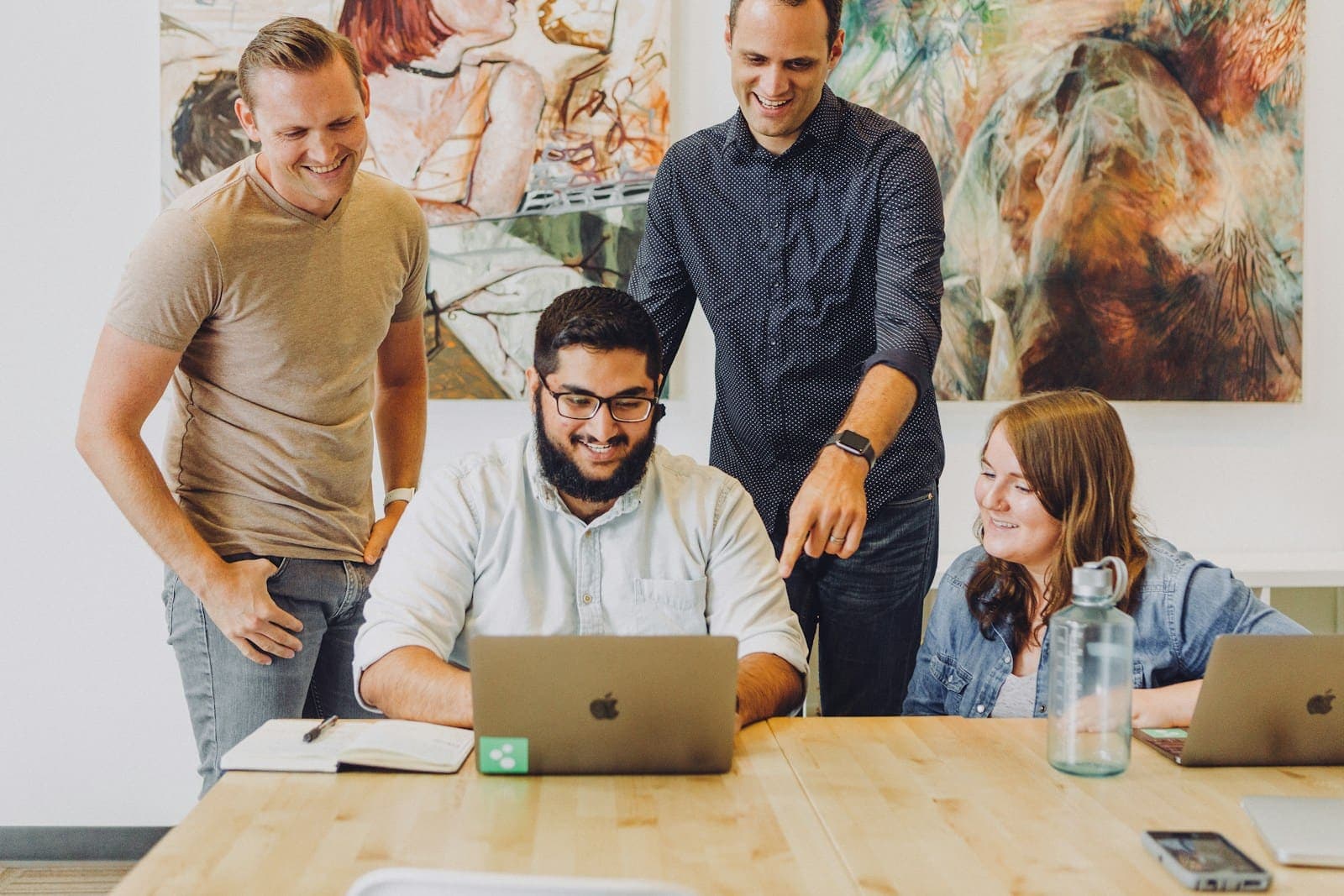 Four colleagues smiling around a laptop at a shared table